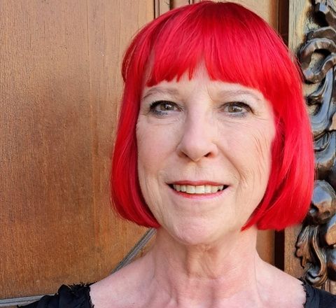A smiling woman with a vibrant, short red bob haircut and dark top.