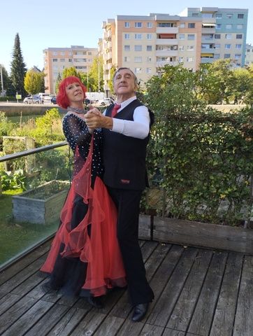 A senior couple dances elegantly on an outdoor balcony with city buildings in the background.